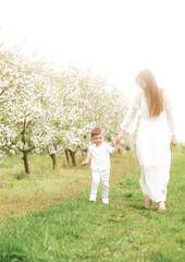 Fototapeta premium Portrait of happy mother and her baby boy. Beautiful touching scene of mom and son. Blooming garden in spring.