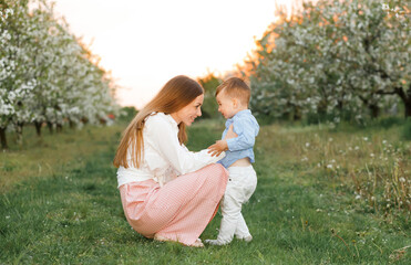 Portrait of happy mother and her baby boy. Beautiful touching scene of mom and son. Blooming garden in spring.