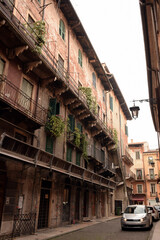 Balconies of an ancient house with several floors in perspective. Under them are modern cars