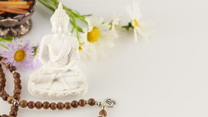 Fototapeta na wymiar Healing and meditation, Energetic health and relax. Buddha statue, prayer beads, aroma sticks and wild flowers on a white background with copy space. Vesak, Buddha Day. Soft image style