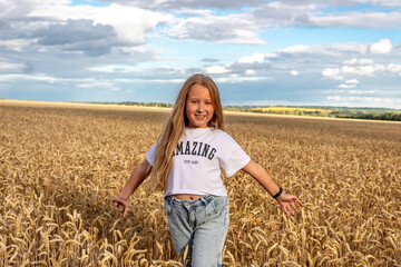 Naklejka na ściany i meble Happy girl with long hair in a wheat field. Sunset. The girl is wearing blue jeans and a white t-shirt.