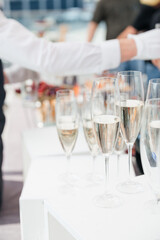 Glasses of champagne for guests at the catering. Exquisite snow-white table. Waiter's hand, luxury elegant holiday service