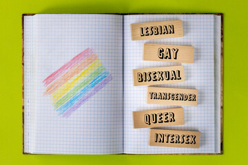 school notebook with hand painted LGBT flag, words written on a wooden block, lesbian, gay, bisexual, transgender, queer, intersex, creative concept for education of tolerance, diversity and equality
