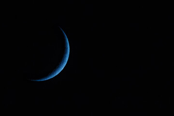 A blue crescent moon in a dark sky © runny1975