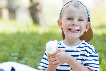Cute, happy little boy with a beautiful smile and dirty face eating ice cream outdoors on a hot summer day. A child enjoys a sweet dessert during the summer holidays.
