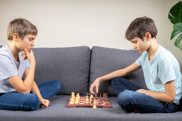 Two brothers are playing chess game while sitting on the couch. Strategic board game, leisure,...