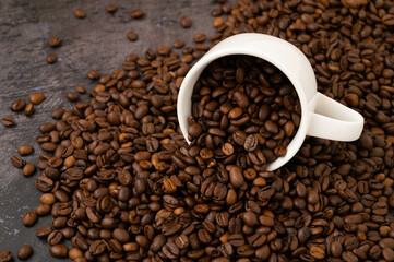 An overturned coffee cup with coffee beans spilled onto a metal surface with coffee beans spilled on it.