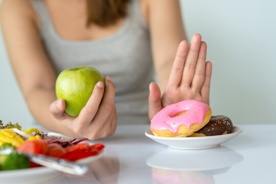 Dieting or good health concept. Young woman rejecting Junk food or unhealthy food such as donut or dessert and choosing healthy food such as fresh fruit or vegetable. - Powered by Adobe