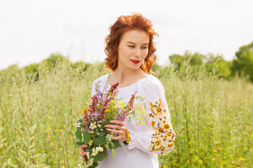 Naklejka na ściany i meble A woman in a Ukrainian embroidered shirt in a field with a bouquet of wild flowers