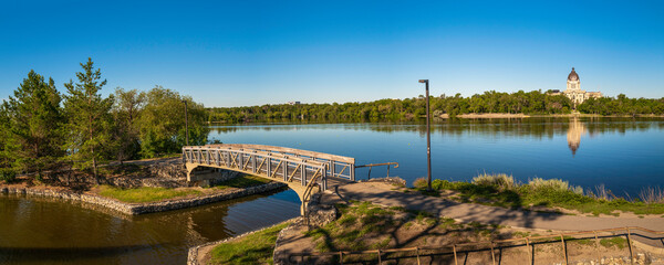Fototapeta na wymiar Tranquil Wascana Lake and the bridge along the walking trail of the lake park in Regina, Saskatchewan, Canada, with a view of the Saskatchewan Legislative Building.
