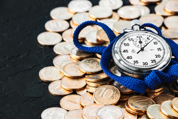 Analog stopwatch and pile of gold coins on a black background close-up. Counting time by stopwatch....