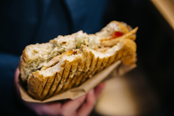 Man holds a hot in his hand bite-sized delicious sandwich with chicken, sauce, and cheese. Closeup