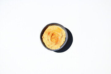 Flat lay of chickpea hummus with sprinkled paprika peppers in blue ceramic bowl on white background with copy ad space