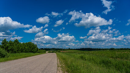 The road in the countryside, the blue cloudy sky and the edge of the road with grass.