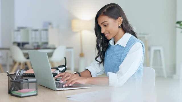 Young woman happily doing business and networking by email on laptop. Professional female is stylish and creative while being alone in office. She is using technology to advance her career