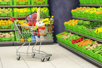 Shopping cart full of food in a grocery supermarket  or grocery store with shelves with fruits and vegetables. © Maksym Yemelyanov