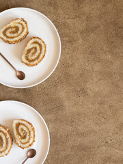 Pieces of biscuit roll with apple jam on a plates next to copper color teaspoons. Brown background, flat lay. Copy space