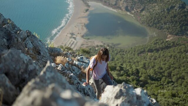 slow motion young woman hiker rock climber climbs up on cliff on mountain over beautiful sea coast in Turkiye. active lifestyle, healthy leisure, outdoors activity by traveling in Turkey at summer