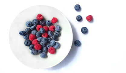 Juicy blueberries and raspberries in a plate close-up on a white background