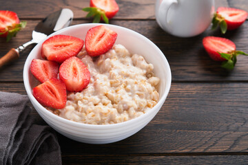 Oatmeal. Bowl of oatmeal porridge with strawberry, almond and milk on old wooden dark table background. Top view in flat lay style. Natural ingredients. Hot and healthy breakfast and diet food.