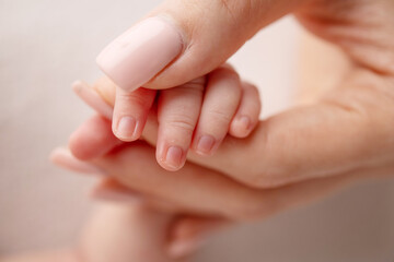 Close-up of a baby's small hand with tiny fingers and arm of mother on a white background. Newborn baby holding the finger of parents after birth The bond between mother and child Happy family concept