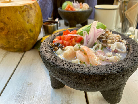 mujer irreconocible comiendo un ceviche en piedra de moler acompa&ntilde;ada de agua de coco, cena marina