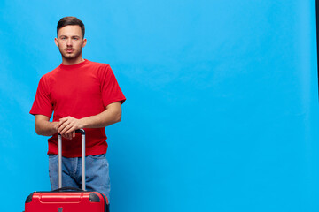 Thoughtful pensive serious tanned handsome man in red t-shirt wait for taxi to airport with suitcase posing isolated on blue studio background. Copy space Banner Mockup. Trip journeys concept