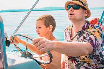 Son and father driving motorboat on holiday. Men teaching a young boy sailing an inflatable rubber...