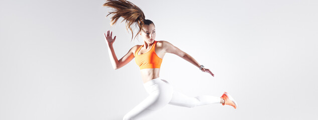 Confident young woman in sports clothing running against white background