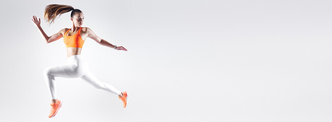 Confident young woman in sports clothing jumping against white background