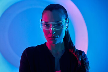 Confident young woman in futuristic glasses standing against colorful background