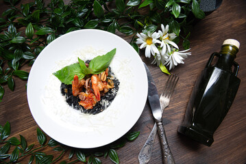 A plate of pasta with cuttlefish ink and seafood, under grated parmesan cheese, garnished with fresh basil leaves. Top view.