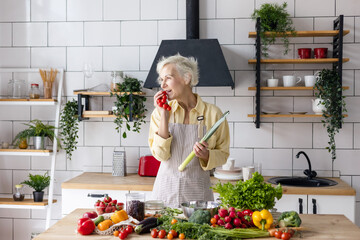 beautiful elderly gray haired senior woman cook in cozy kitchen with fresh organic vegetables,...