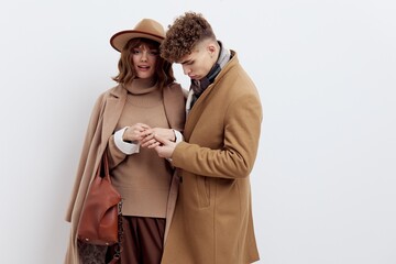 a beautiful couple in love is standing on a white background in autumn clothes and holding hands sweetly, a woman has an autumn hat on her head and a bag in her hand