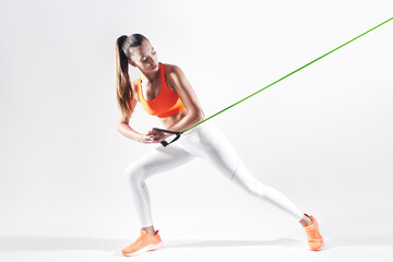 Fototapeta na wymiar Confident young woman using resistance band while exercising against white background