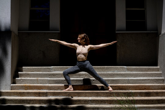 young woman performing yoga in front of house