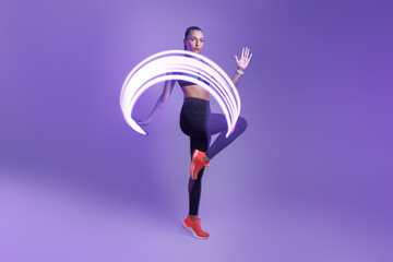 Confident young woman in sports clothing exercising against violet background