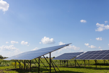 Solar panels in a field against a cloudy blue sky on a sunny day.