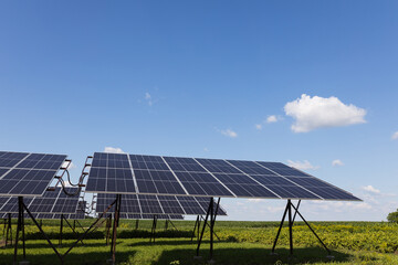  Solar panels in a field lined up against a cloudy blue sky on a sunny day.