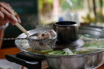 Selective focused, dipping slice of fish in metal strainer into boiled soup inside hot pot. 