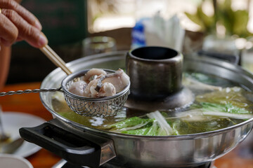 Selective focused, dipping slice of fish in metal strainer into boiled soup inside hot pot. 
