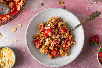 Delicious strawberry crumble with almonds and pumpkin seeds in a plate on pink background. Top view