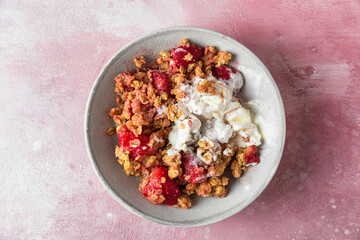 Delicious strawberry crumble with ice cream, almonds and pumpkin seeds in a plate on pink background. Top view