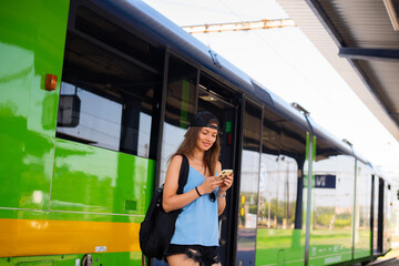A young athletic woman stands with a smartphone near the train at the railway station.