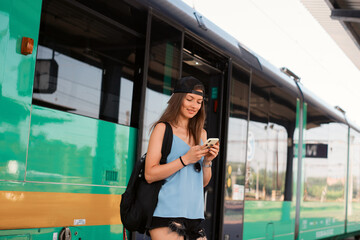 A young athletic woman stands with a smartphone near the train at the railway station.