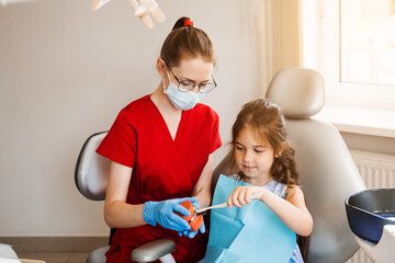Dentist shows child how to properly use toothbrush for brush teeth. Jaw anatomical model teeth...