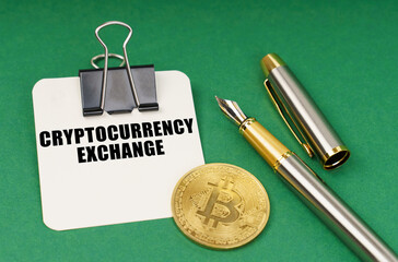 On a green surface, a bitcoin coin, a pen and a sheet of paper with the inscription - Cryptocurrency exchange - Powered by Adobe