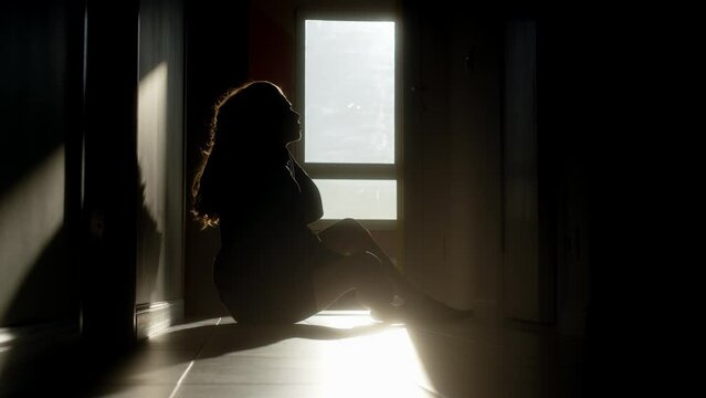 Silhouette of frustrated woman with long hair sitting in corridor at sunrise or sunset. sun illuminates girl who broke off relations with man. drama or abuse in family with difficulties and problems.