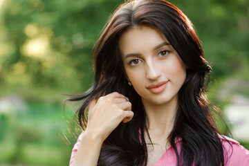 Closeup portrait of a brunette with wavy hair, wearing a pink dress in the park