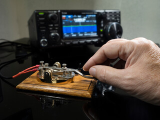 Selective focus of man's hand on a telegraph key with radio defocused in background - obrazy, fototapety, plakaty